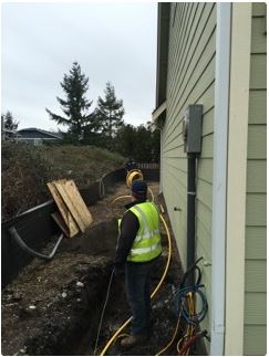 Construction worker in safety vest near a house, working on buried utilities.