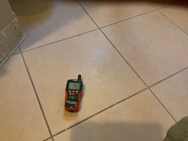 Orange meter displaying 902 rests on tan tile floor with dark grout lines.