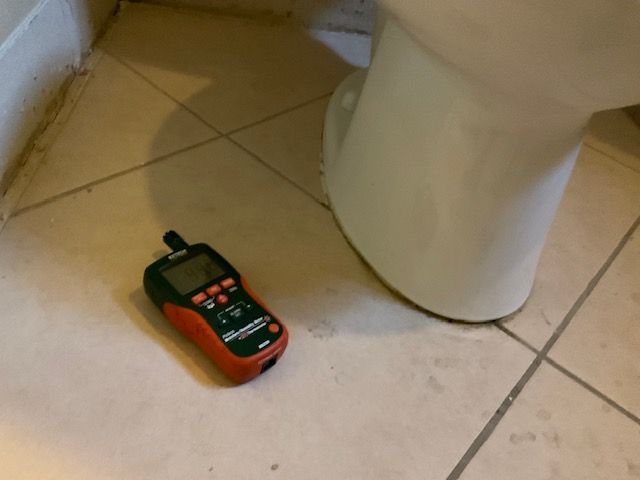A moisture meter on tiled floor next to a white toilet.