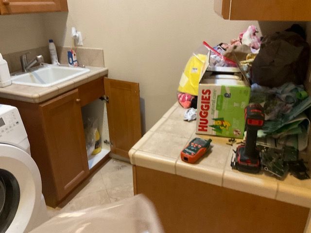 Laundry room with a sink, open cabinet, and cluttered countertop with a box of diapers.