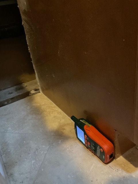 Laser measuring tool at the base of a brown wall, on a tiled floor.