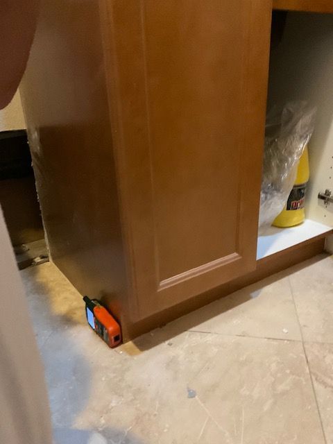 Orange laser level on floor next to brown cabinet base.