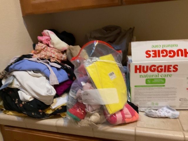 Clothes pile, bag of items, and Huggies wipes box on a counter.