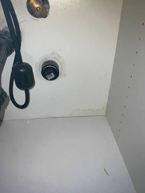 Under-sink cabinet showing plumbing pipes and water damage on the back and base.