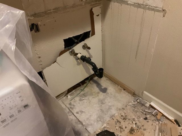 Damage to wall around plumbing with exposed pipes in a room under construction.
