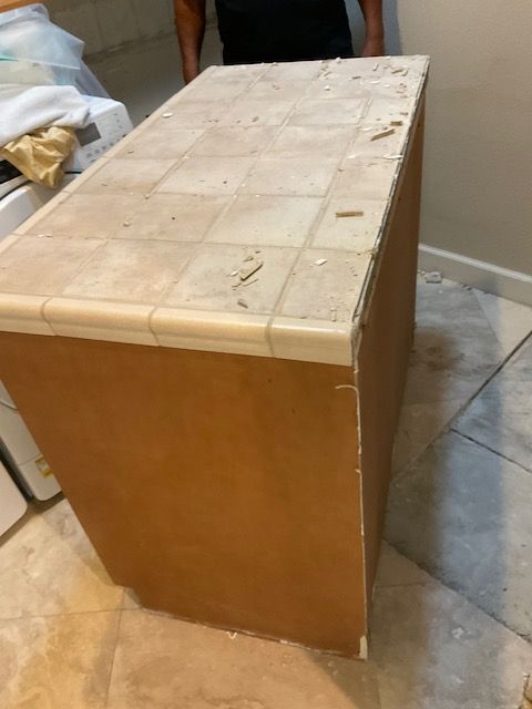 A kitchen island with a tile countertop and light brown cabinets. A person stands behind it.