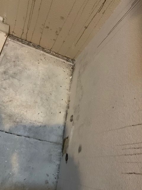 Concrete room corner, walls and floor stained, some vertical streaks on walls.