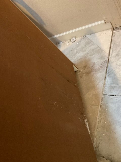 Brown cabinet next to white trim and light-colored tiled floor, possibly in a corner.