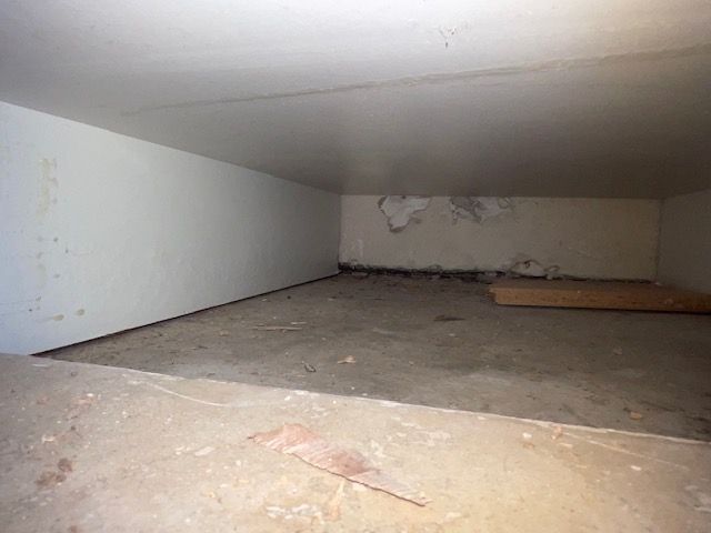 Interior view of a small, rectangular room with concrete floor and white walls. Some water damage is visible.