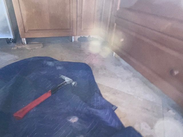 Hammer on blue tarp in front of kitchen cabinets. Light brown cabinets, debris on floor.