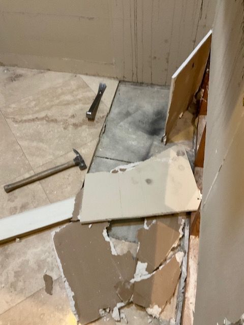 Renovation in progress: Torn wall, tile debris, hammer, and pry bar on the floor.