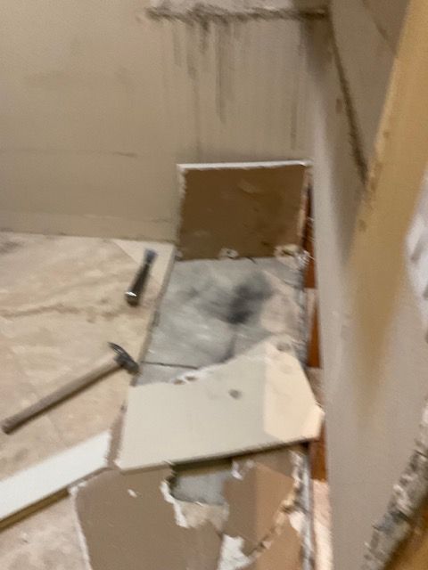 Demoed bathroom with tools, debris, and exposed wall. Beige, white, gray colors.