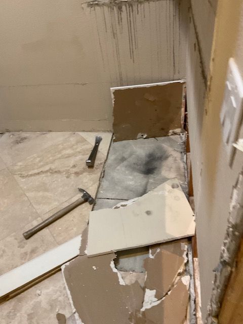 Demolition in a room: damaged drywall, broken tiles, hammer, chisel lie on floor.