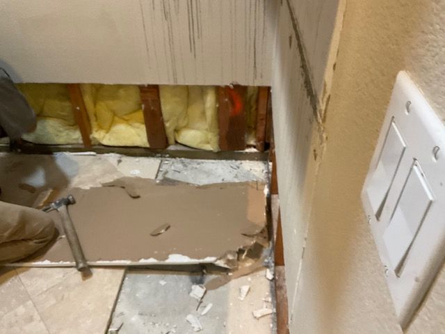 Construction: Damaged wall with exposed insulation. Person demolishing sheetrock next to light switch.