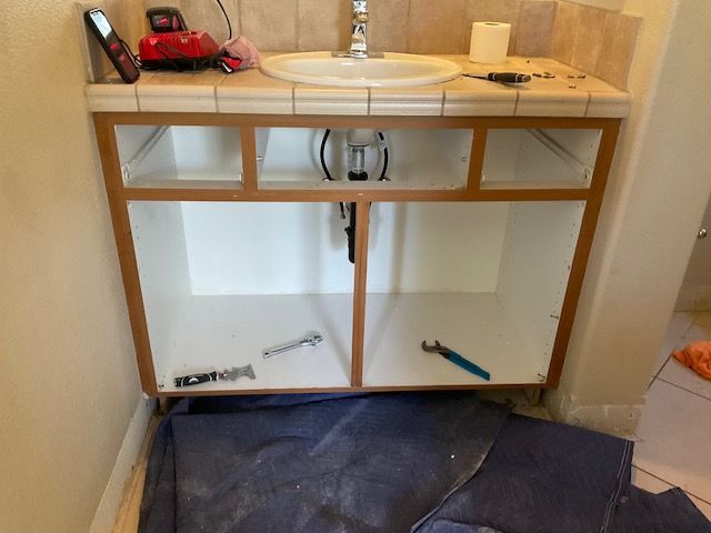 Bathroom vanity with open cabinet doors, tools inside, and sink in a tan setting.