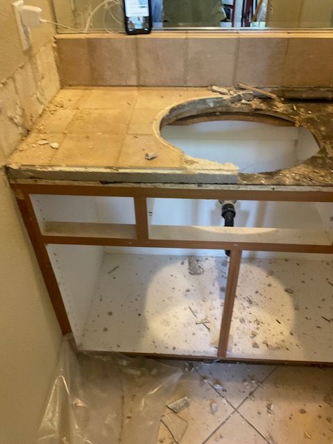 Bathroom vanity under construction: countertop removed, sink hole, open cabinet, debris.