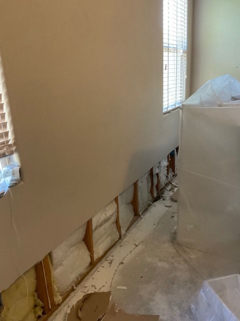 Interior wall with exposed studs, damaged drywall, and a covered object near a window.