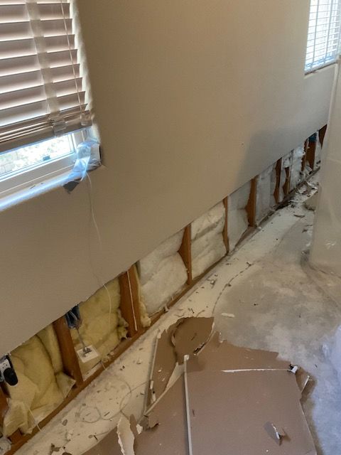 Exposed wall studs with insulation, damaged drywall, and a window in a room.