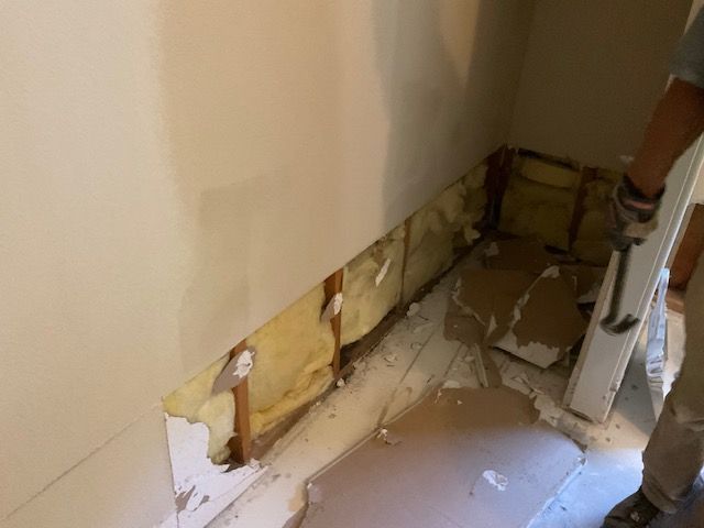 Man removing drywall from a wall section near a doorway. Yellow insulation is visible.