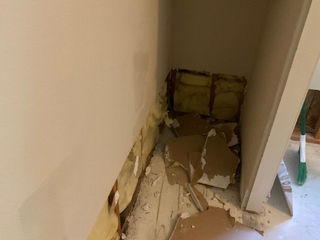 Interior wall demolition, exposing insulation and debris in a corner.