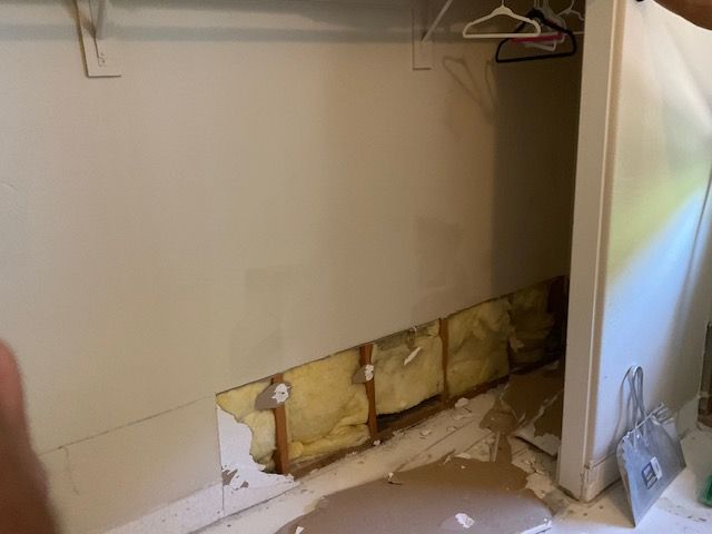 Closet with damaged drywall exposing insulation and wooden framing.
