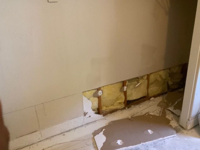 Wall with missing section exposing insulation, near doorway, interior shot.