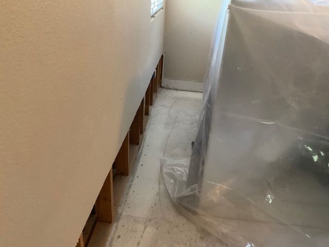 White room, exposed wooden studs along wall base. Appliance covered in plastic.