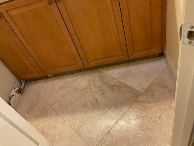 Light-toned tiled floor in a room with wooden cabinets and a partially visible doorway.