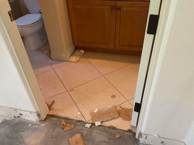 Bathroom doorway with damaged floor tiles and debris.