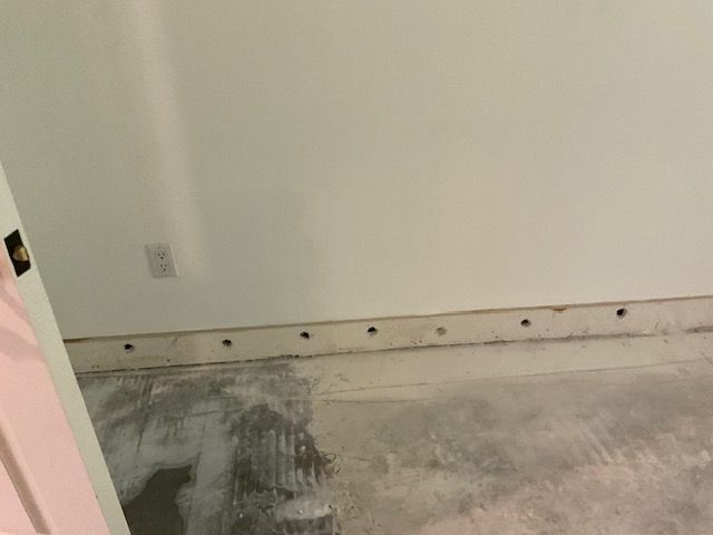 Bare concrete floor with holes along the wall. White walls and a partially visible doorway.