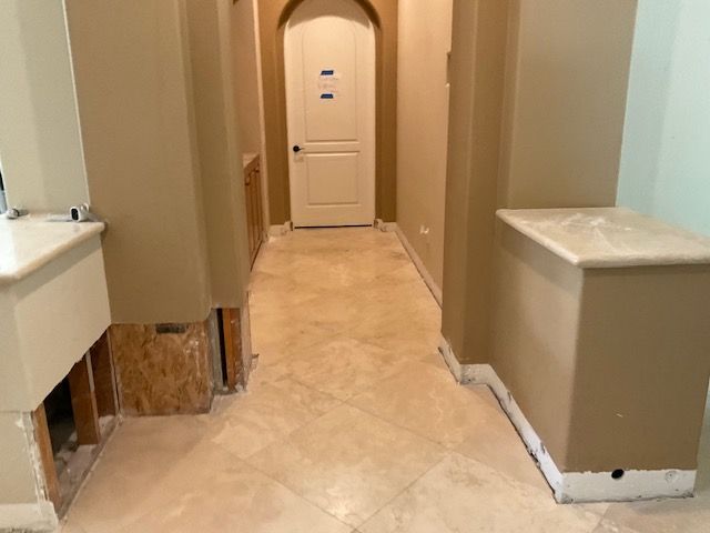 Hallway with beige tile floor and tan walls. Exposed cabinetry base. Door at end of hallway.