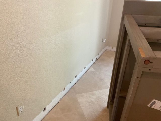 Beige wall with baseboards, a partially visible wooden table, and beige flooring.