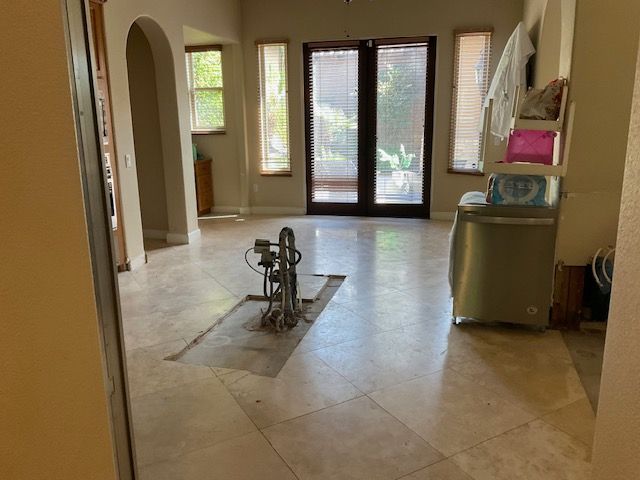 A room with tile flooring and an exposed pipe system; a washing machine sits near the door.