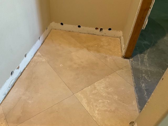 Tiled floor with tan tiles, corner of a room with walls and doorway, unfinished trim.