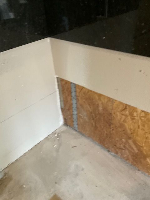 Corner of a room under construction with exposed wood paneling and drywall.
