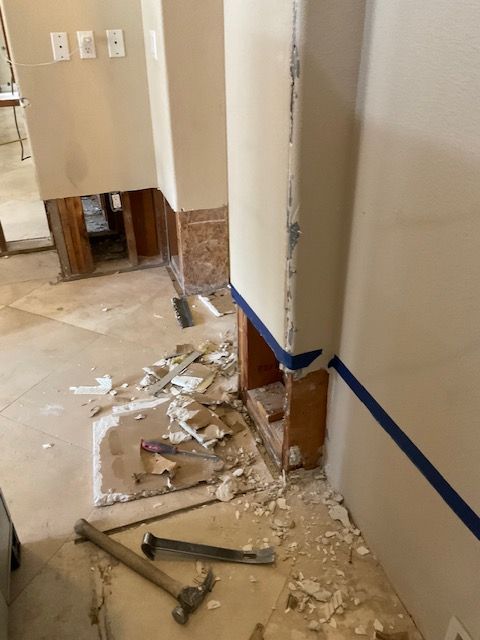 Renovation in progress; torn up flooring, debris, exposed wall studs, and tools lie on the floor.