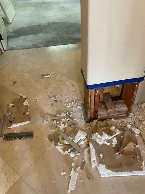 Debris scattered around a support column. Construction or renovation in progress on tiled floor.