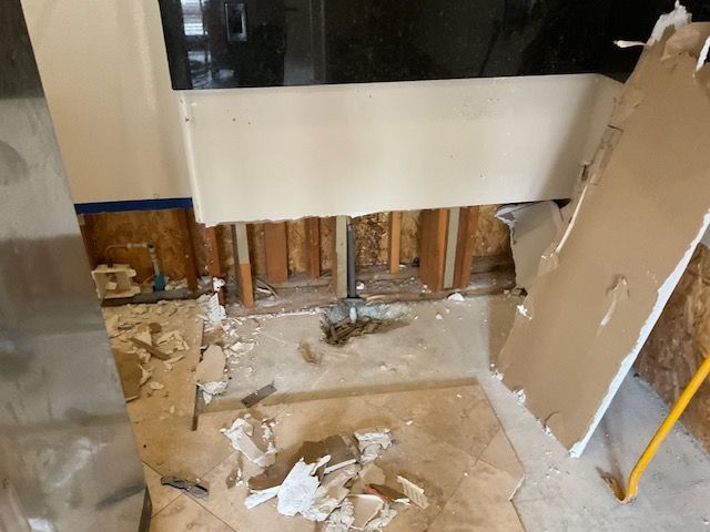 Bathroom undergoing renovation, with exposed framing, torn drywall, and debris on the floor.