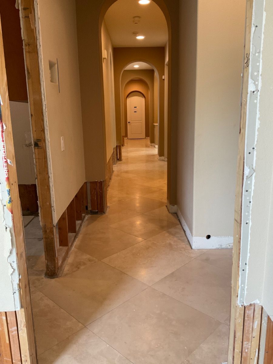 Long hallway with arches, beige walls, and tiled floor. Construction with exposed wooden frame.