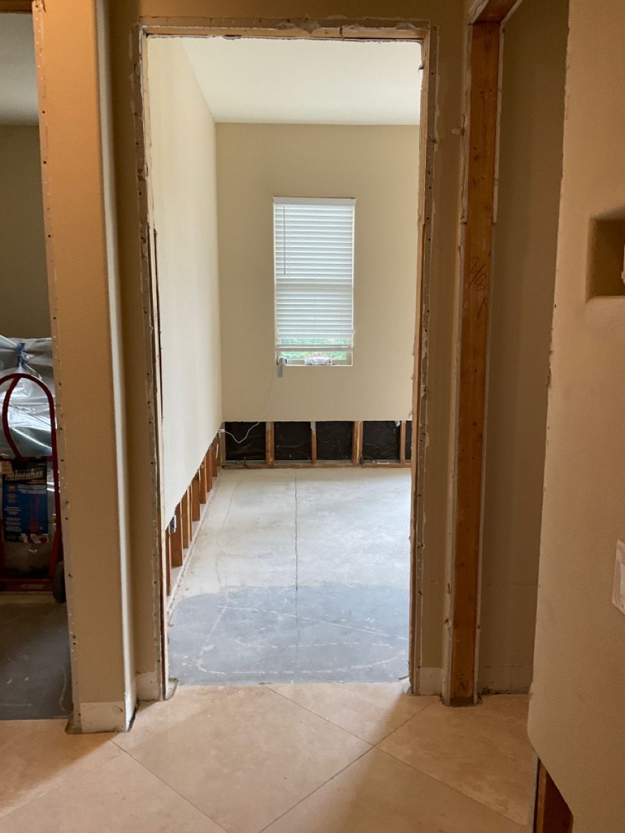 Interior doorway opening to a room under renovation; exposed wall studs, concrete floor, small window.