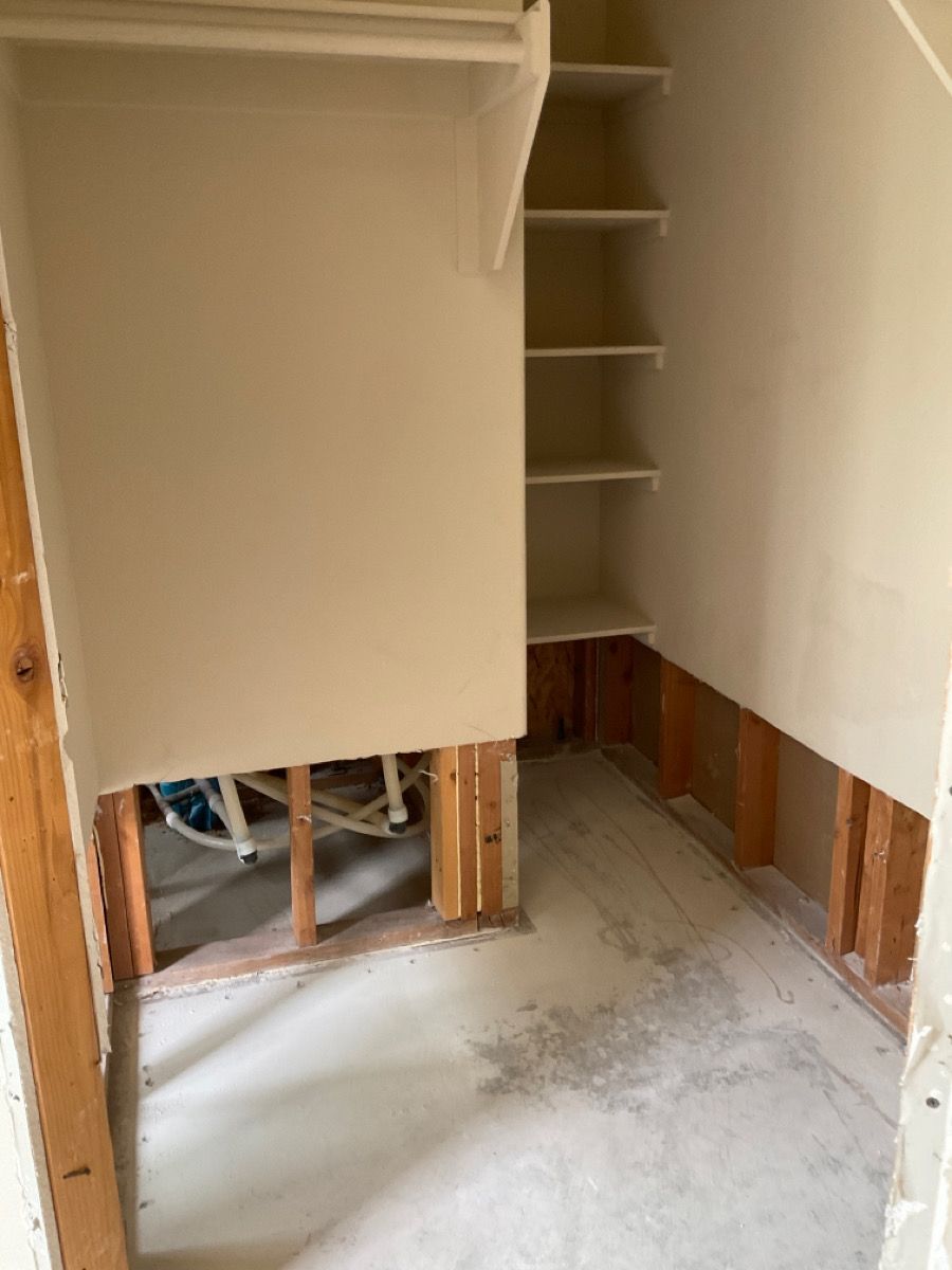 A closet under construction with exposed studs and shelves. Beige walls and concrete floor.
