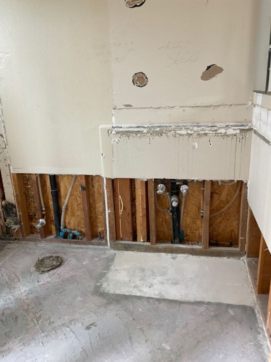 Interior wall under construction showing exposed studs, plumbing, and cement flooring.