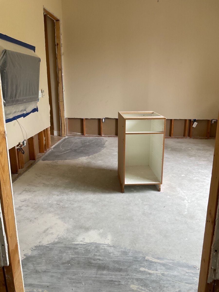 Interior view of a room under renovation with a cabinet, exposed walls, and concrete floor.