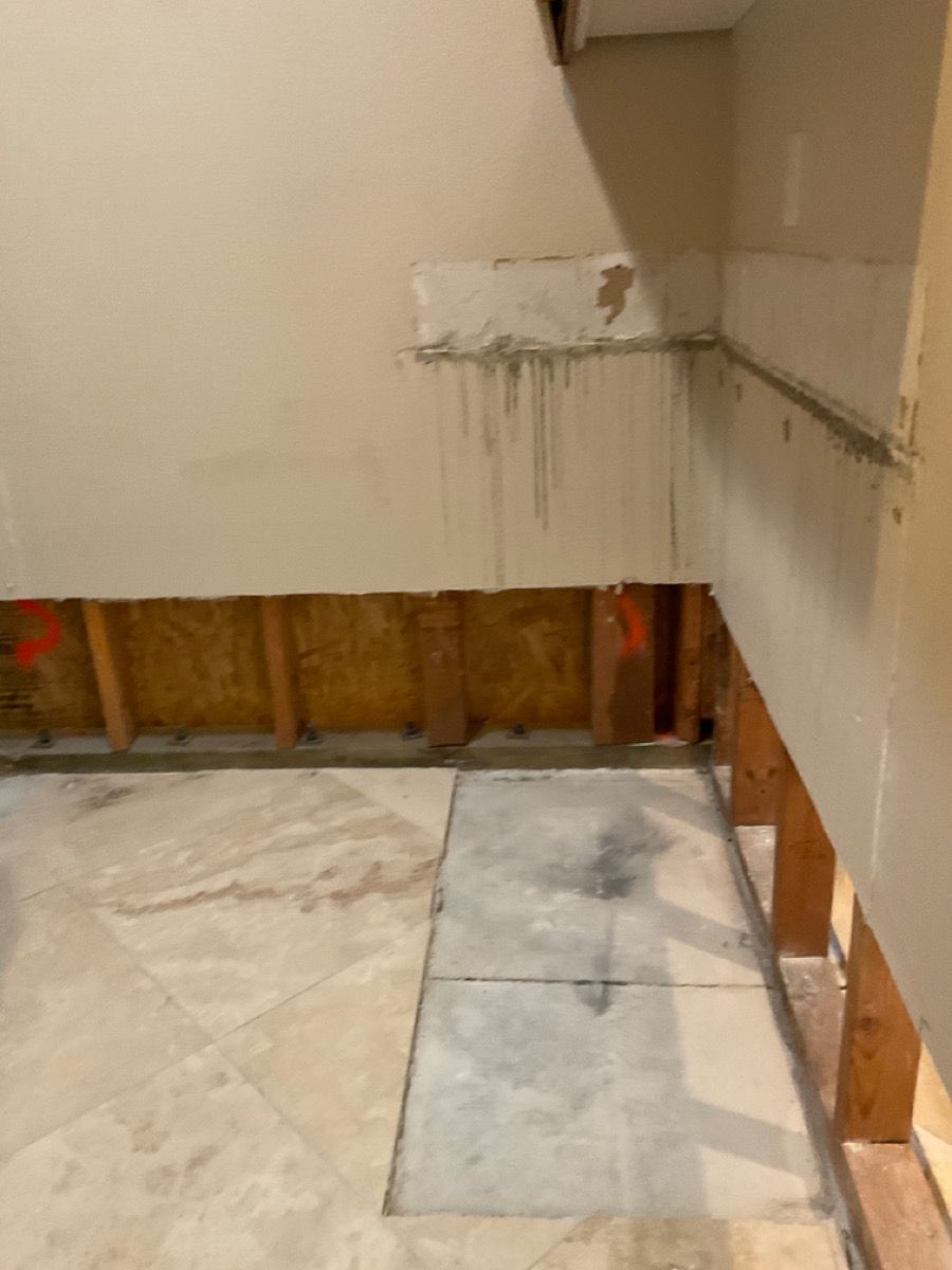 Water-damaged wall, exposed framing, missing drywall, and stained floor tiles.