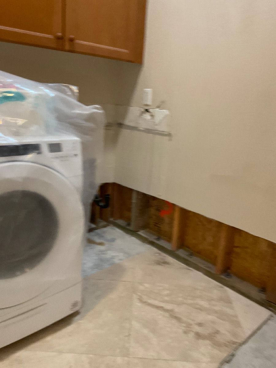 Laundry room with exposed wall studs, washing machine, and water damage on floor.