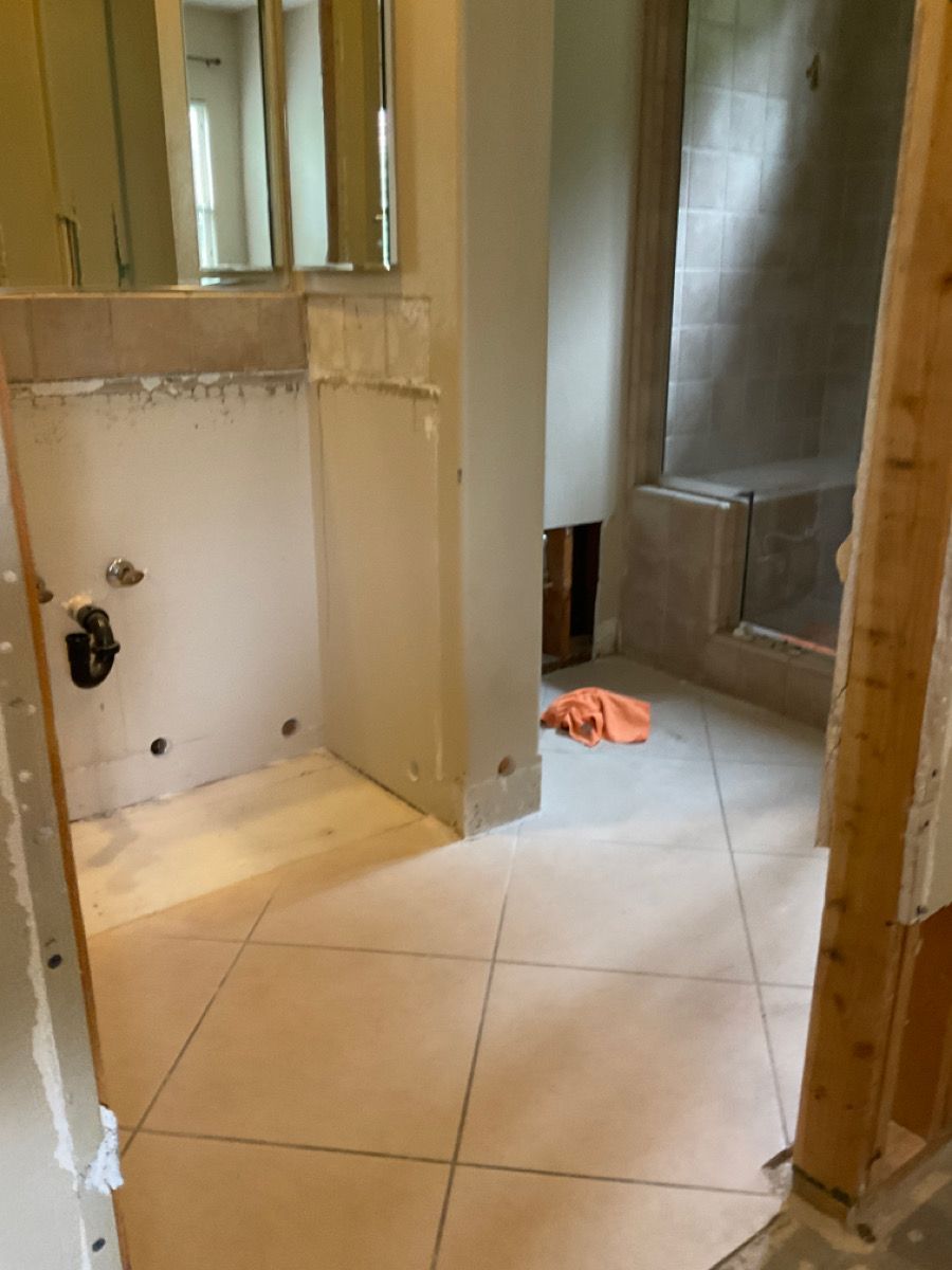 Bathroom under renovation with beige tile floor, partially tiled walls, and shower stall.