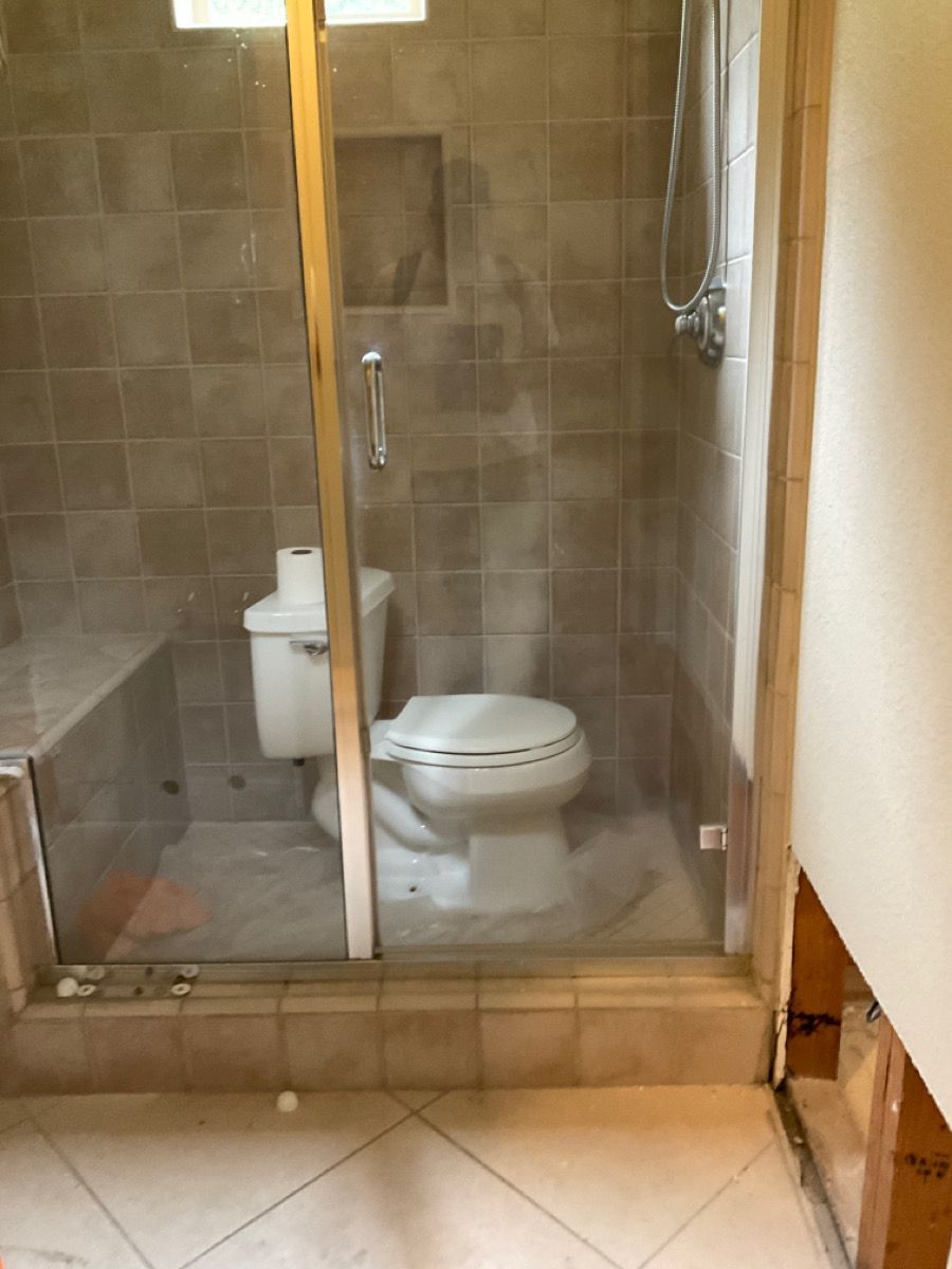 Bathroom: Toilet inside shower stall with glass door, light brown tile.