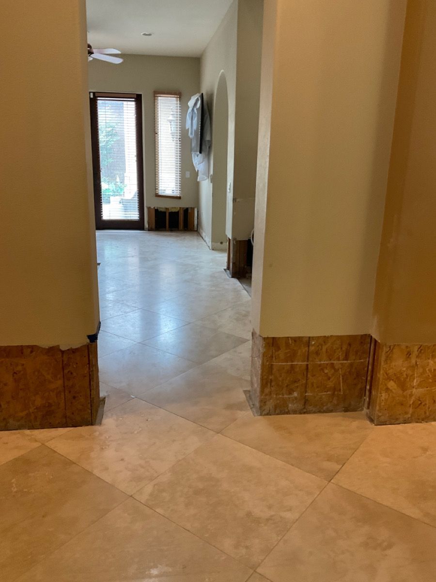 Hallway with beige tile floor, pillars, and door to the outside. Brown tile baseboards.