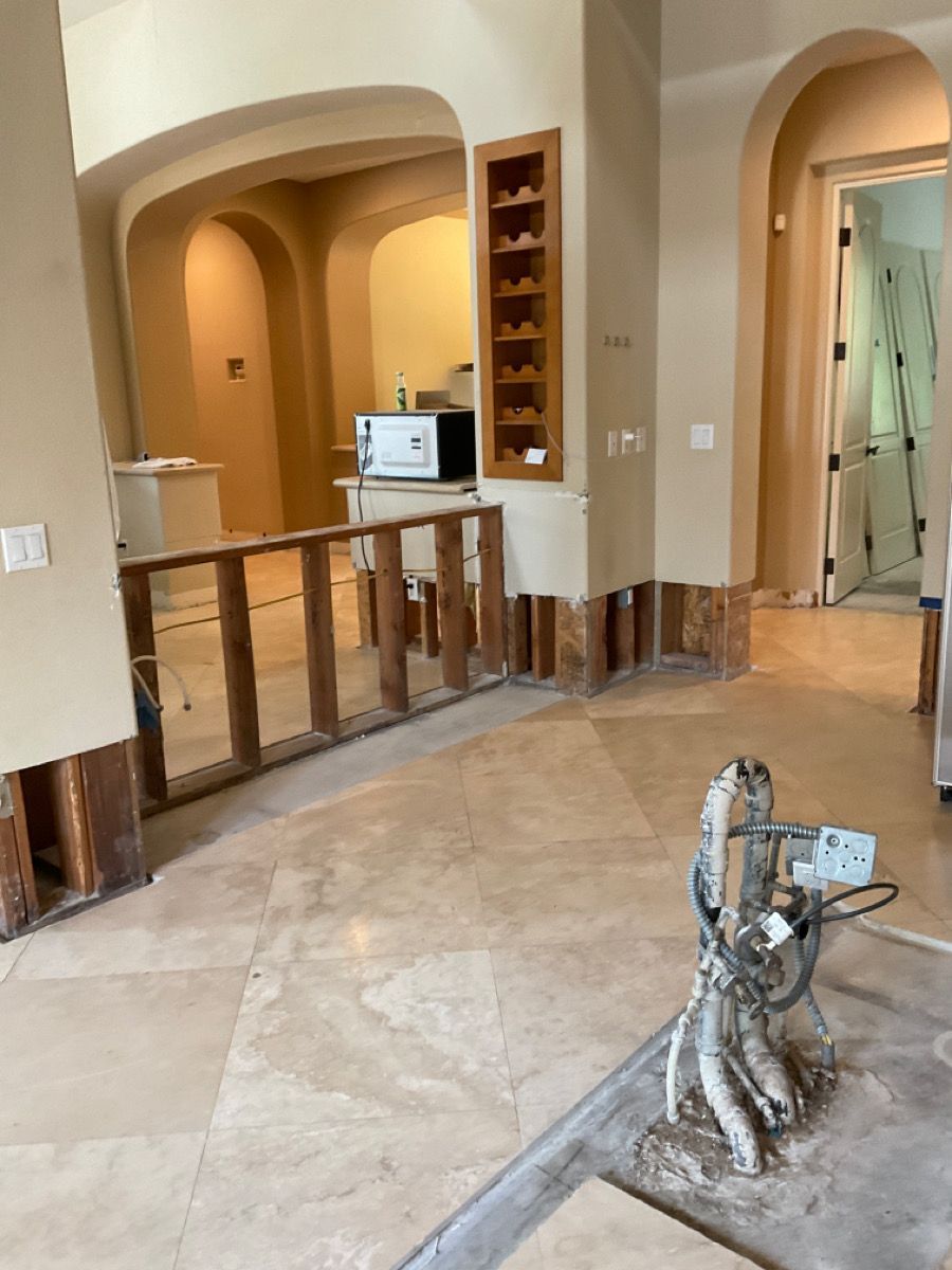 Renovation: Beige room with partial wall removed; exposed wood framing, beige tile floor, and arched doorways.