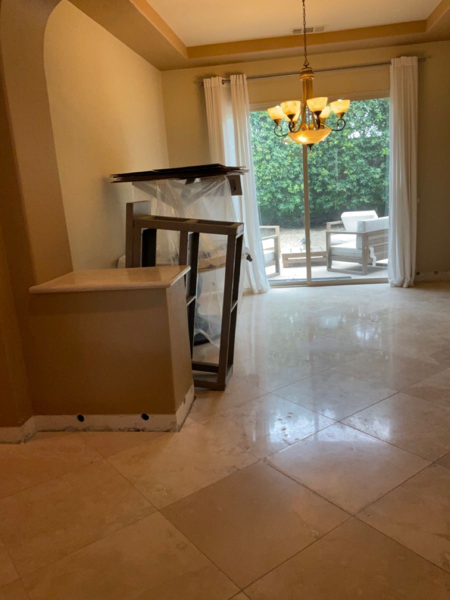 Empty dining room with tiled floor, large window, chandelier, and a piece of furniture.